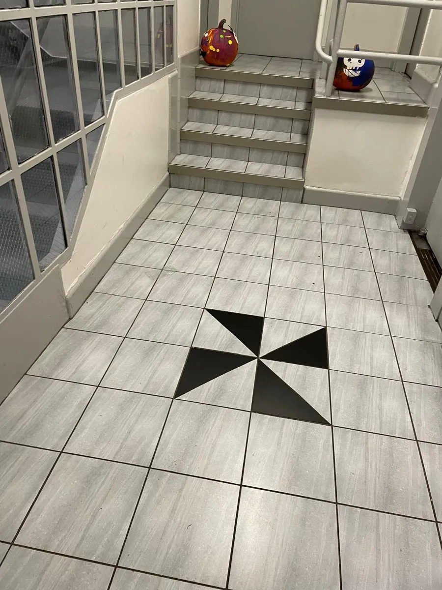Grey plank-look tile floor with a black pinwheel inlay at the foot of a staircase