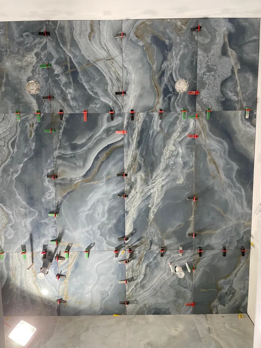 Large blue marble-look porcelain wall tiles being set with leveling clips