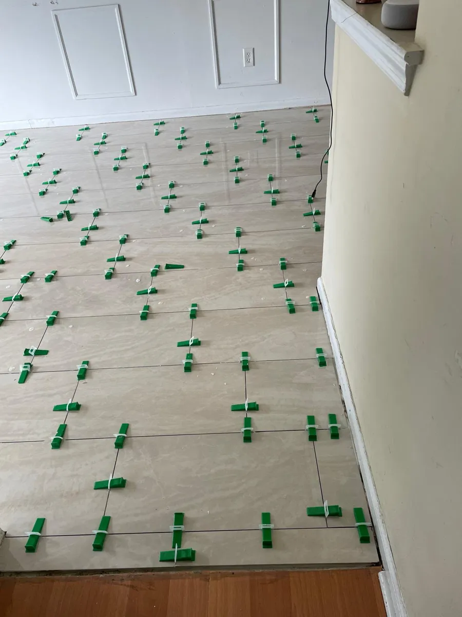 Large light porcelain floor tiles being laid in a hallway with leveling clips