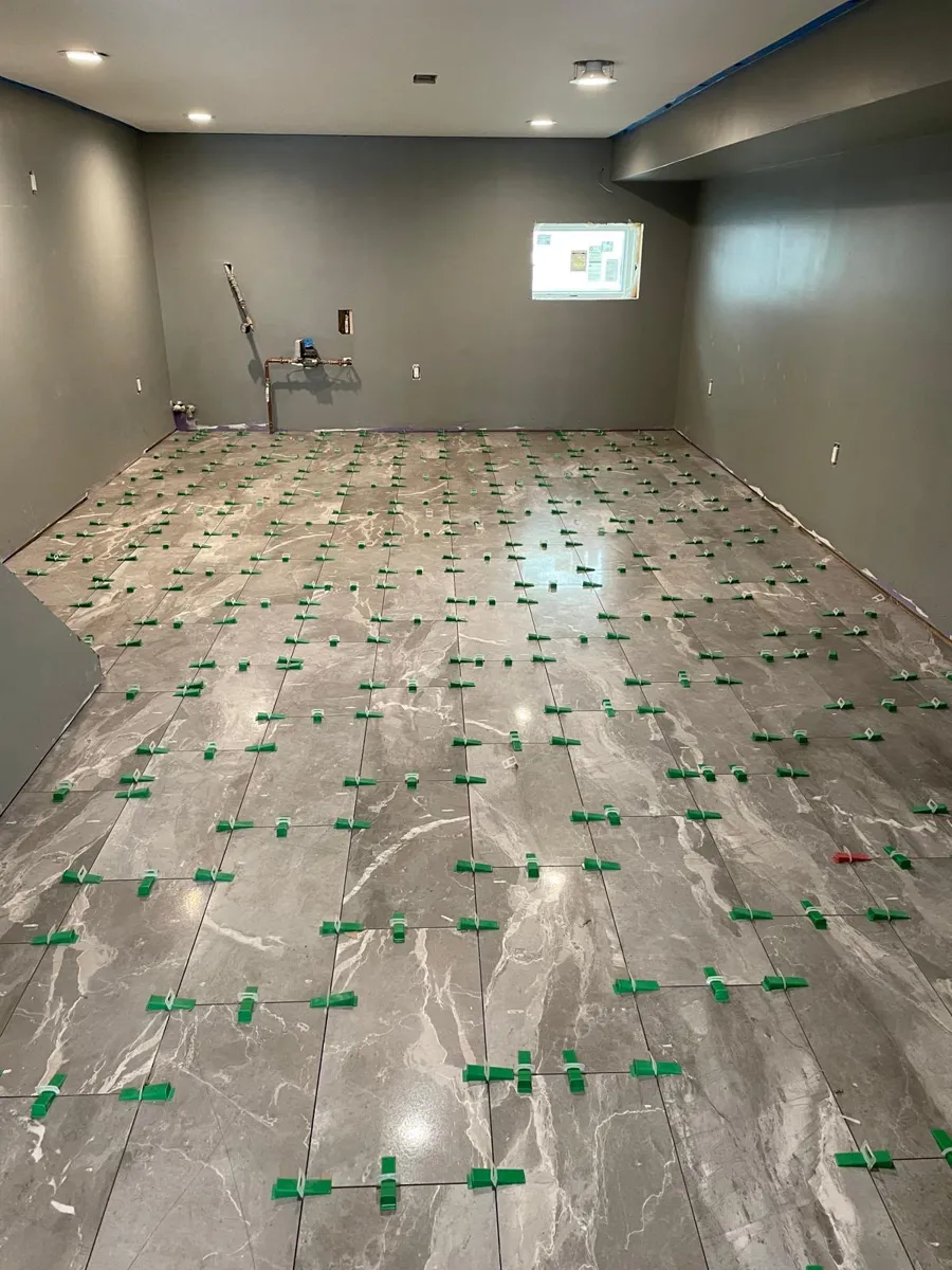 Grey marble-look porcelain floor tile being laid in a large room with leveling clips