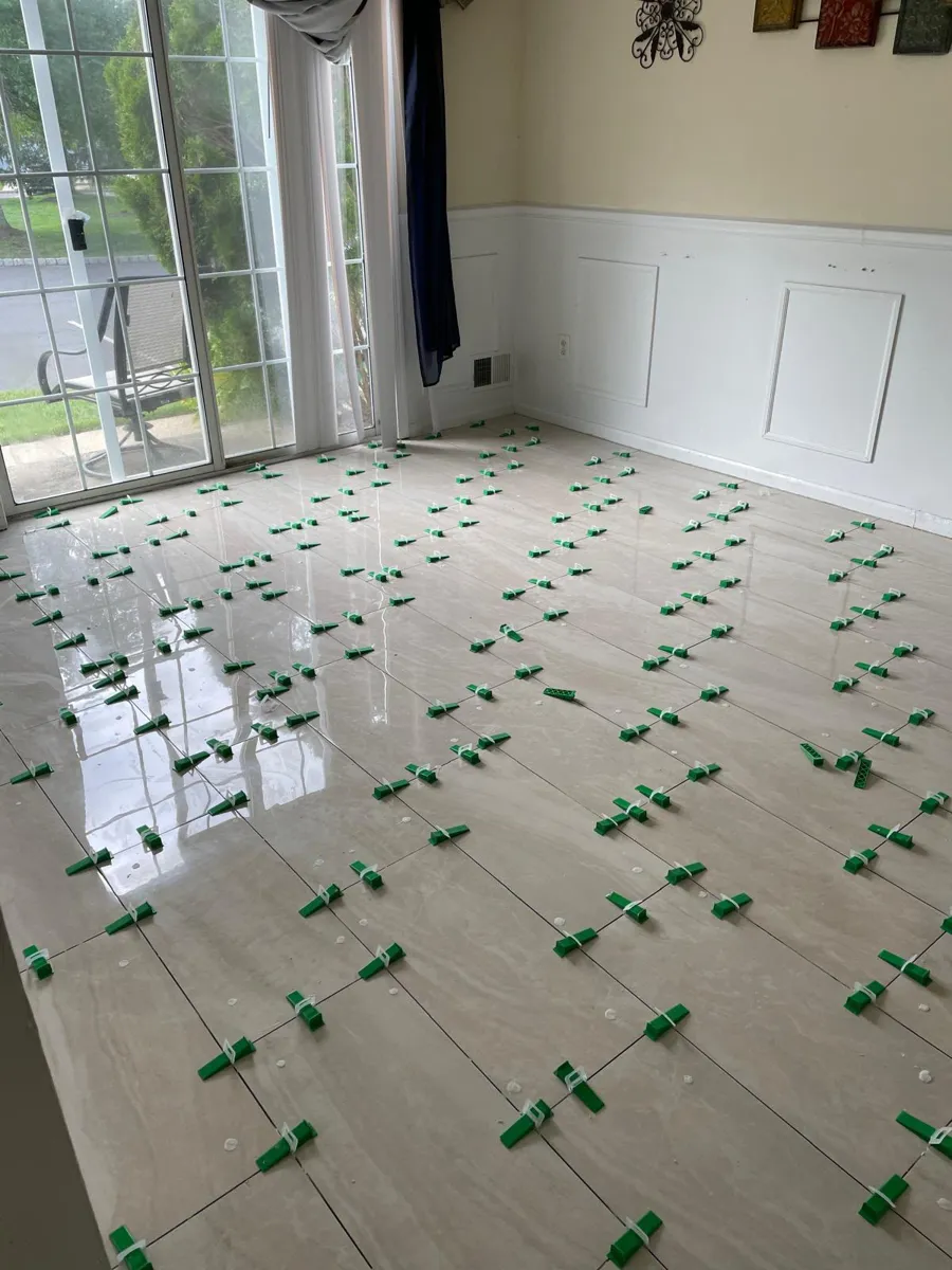 Glossy light porcelain floor tile being leveled in a living room with sliding doors