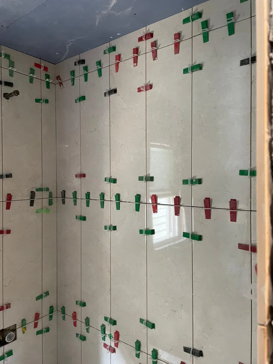 Tall cream porcelain wall tiles being installed with leveling clips
