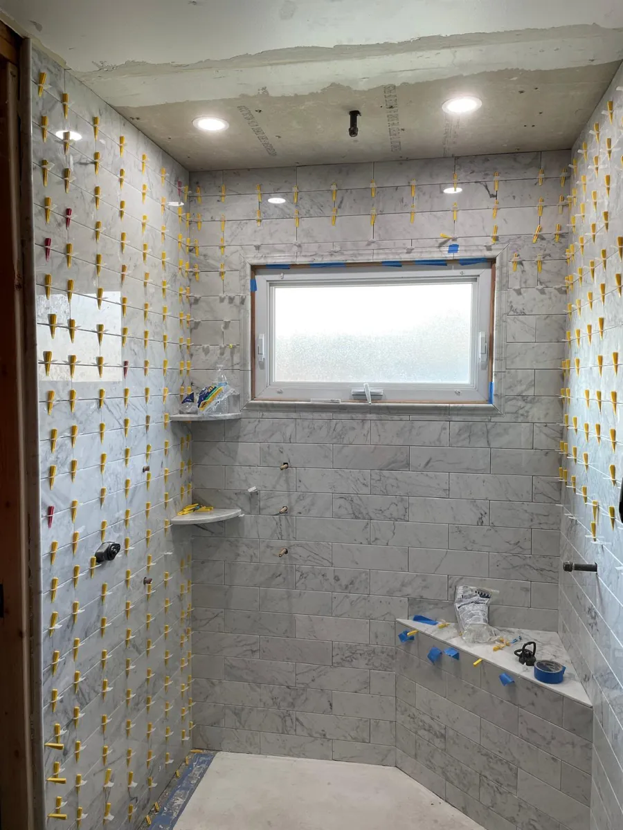 Shower with white marble-look subway tile walls, shelves and a bench being installed