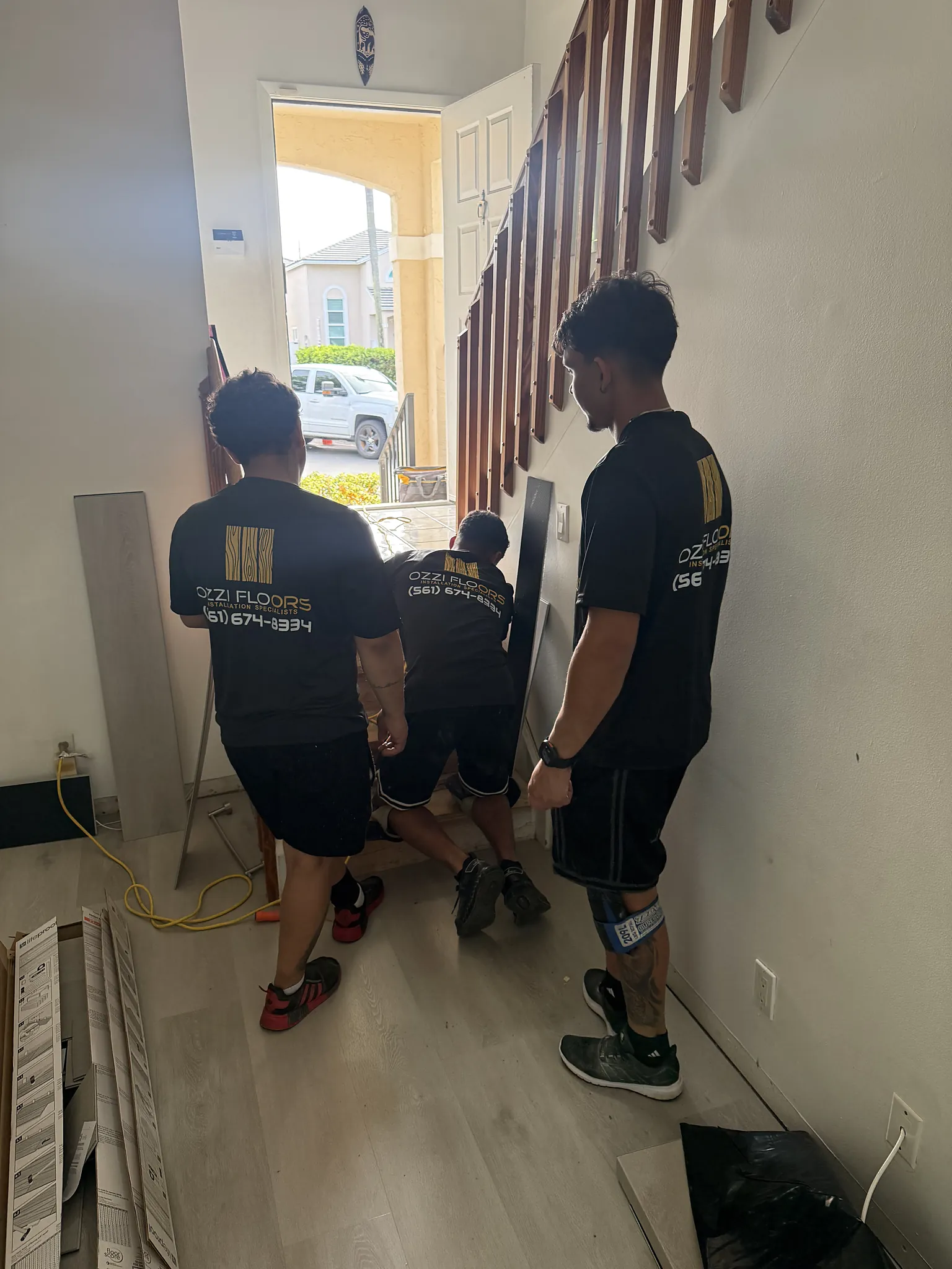 Three Ozzifloors installers carrying material into a home past the staircase