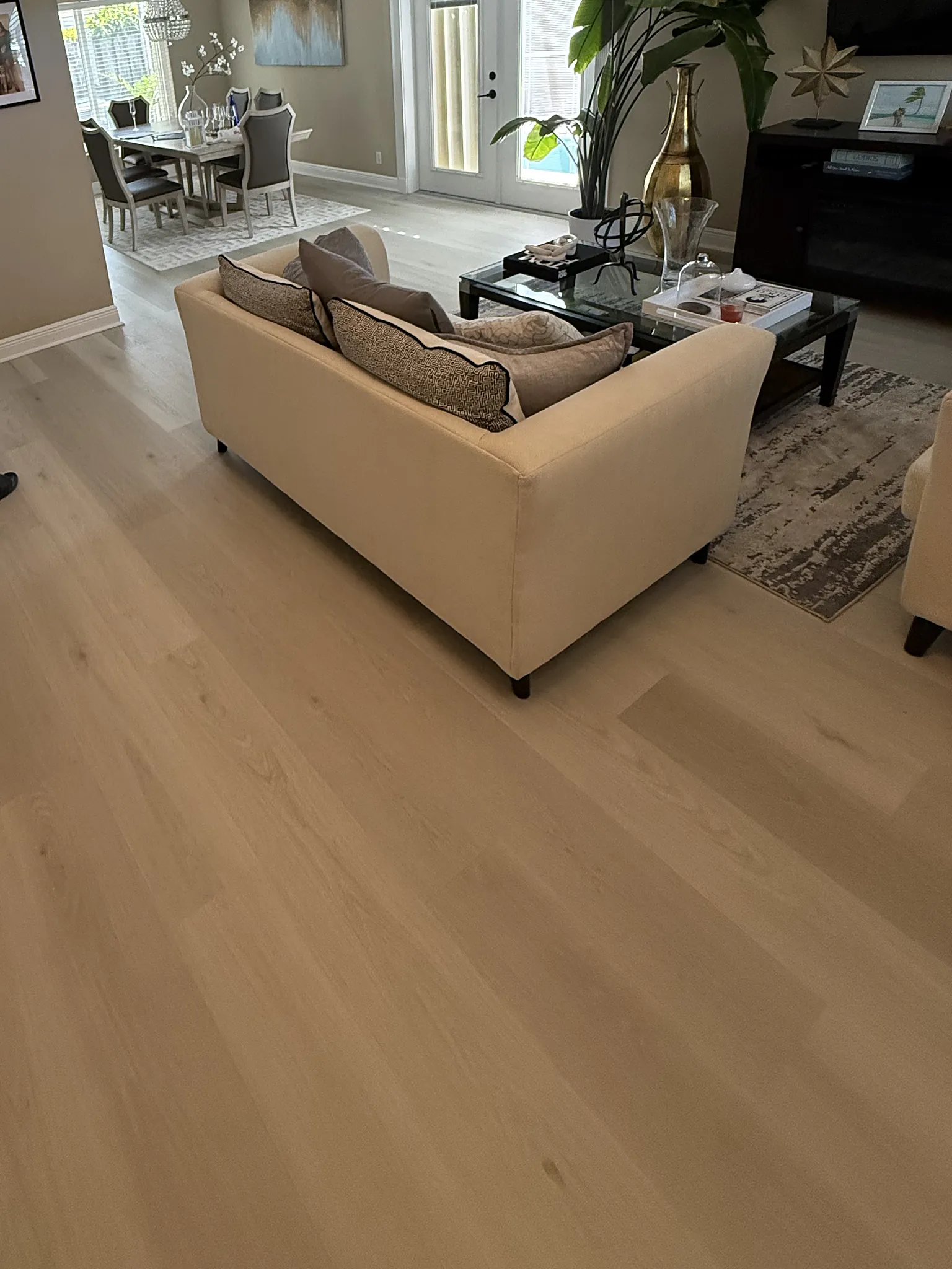 Light plank flooring through a living room, with the dining area beyond